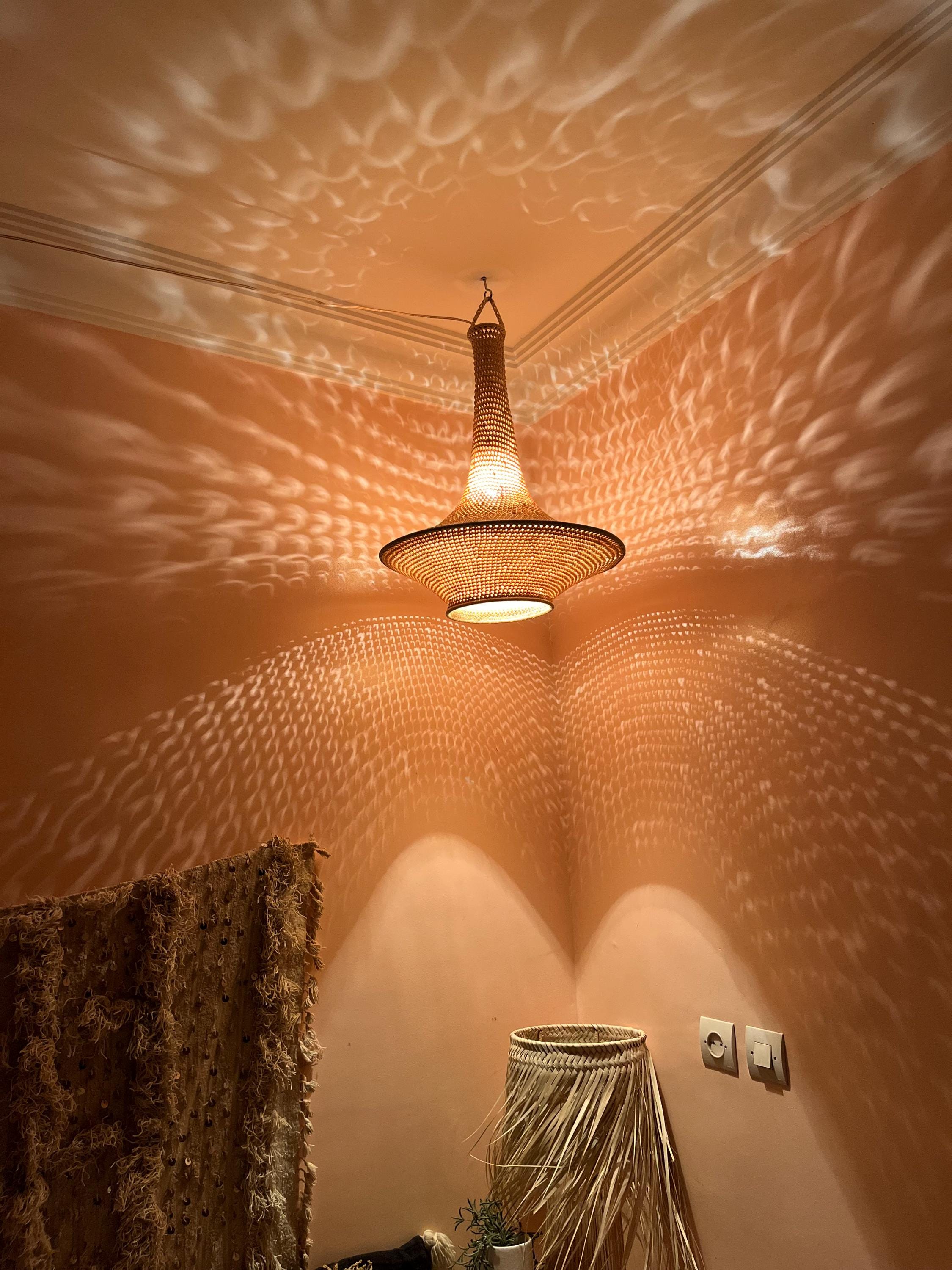 A woven pendant light fixture with a conical top and a wide, circular base hangs from the ceiling. The light casts a…